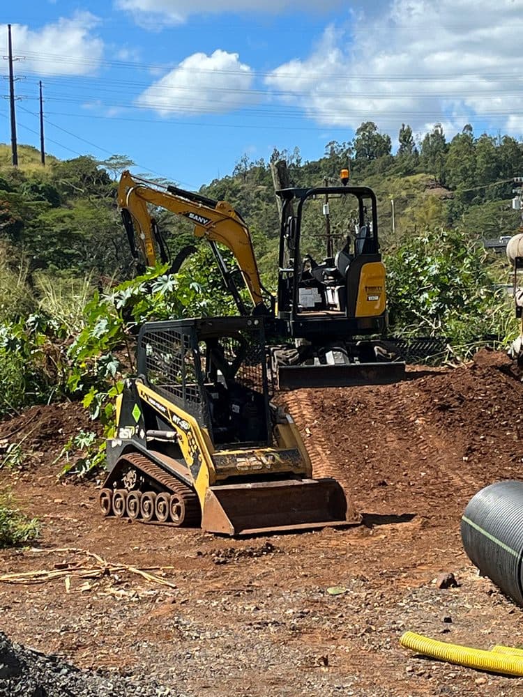 Excavator and skid steer opening ground for septic drainfield work on O'ahu — Alpha Omega Plumbing