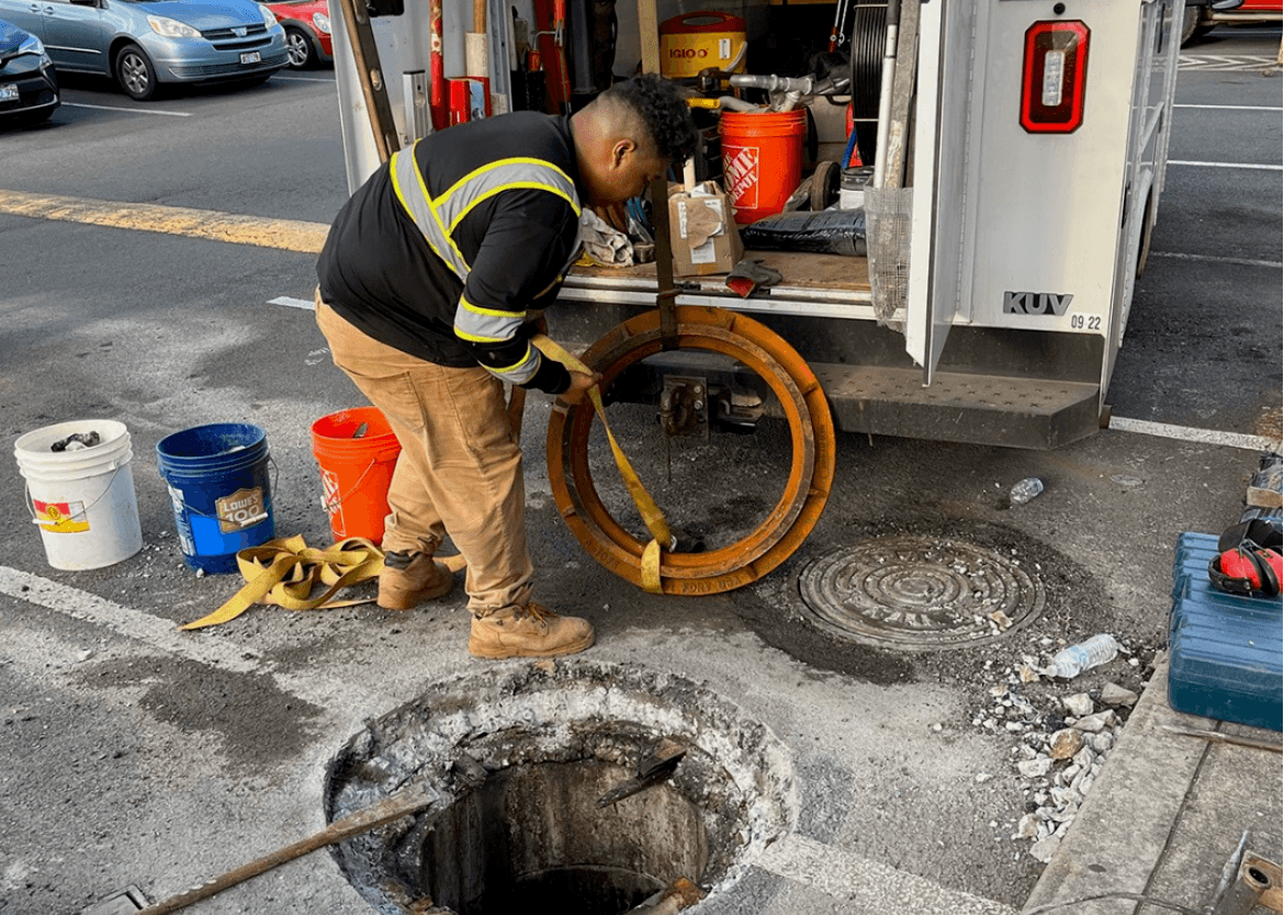 Alpha Omega Plumbing technician working at a street sewer access point during a sewage backup call on O'ahu